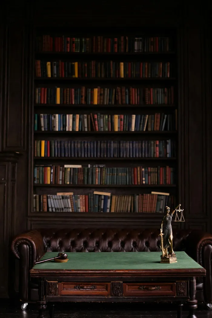 Dramatic law library with leather sofa, wooden bookshelves, and Lady Justice statue